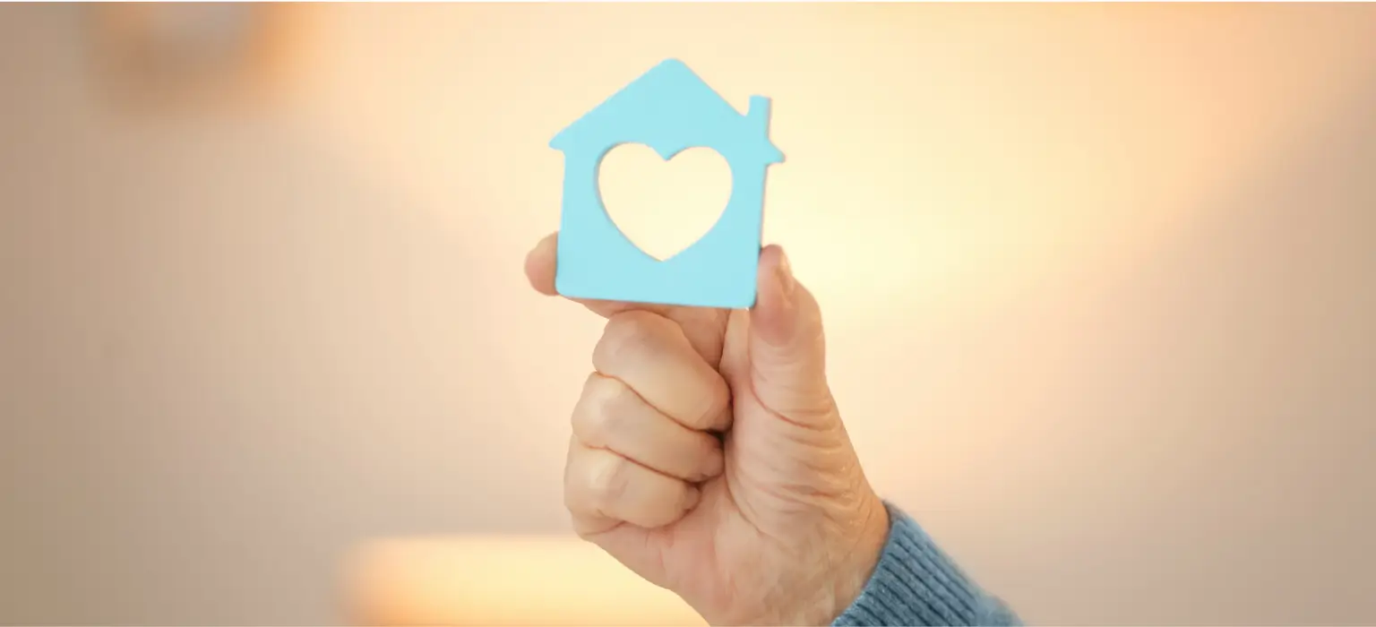 Hand holding blue house with heart and Vanderburgh Sober Living wreath icon symbolizing safe sober living home